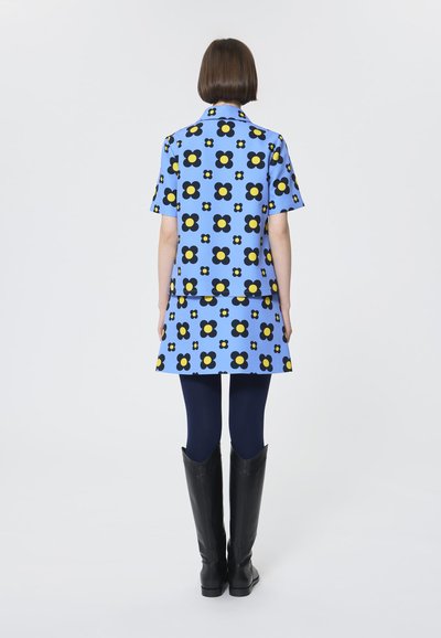 Blaues blumengemustertes Kleid mit kurzen Ärmeln, das mit schwarzen und gelben Blumen verziert ist. Kombiniert mit marineblauen Leggings und kniehohen schwarzen Stiefeln.