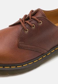 Braune Leder-Schuhe mit runder Zehenform, ausgestattet mit braunen Schnürsenkeln, Messing-Ösen und gelben Nähten entlang der schwarzen Gummisohle.