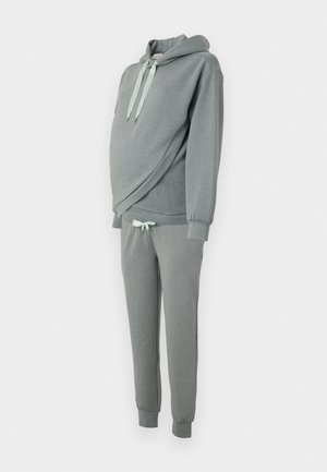 Sudadera gris con capucha y cordones en verde menta, combinada con pantalones de chándal a juego con corte tapered, que cuentan con una cinturilla elástica y puños.