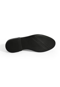 Zwarte schoenzool met een gladde oppervlakte, gestructureerde grippatronen en diagonale groeven voor grip. Plat met een ronde neus en een minimalistisch ontwerp.