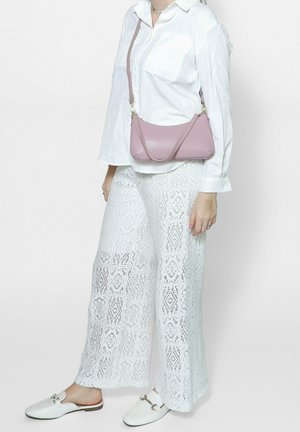 Witte kanten wijde broek met vierkantpatroon, gecombineerd met een lange mouwen witte blouse en een kleine roze leren schoudertas. Witte instappers.