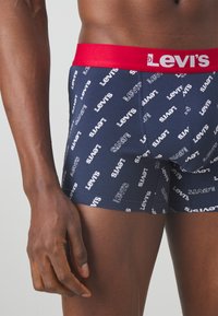 Mörkblå boxershorts med vitt "Levi's" logomönster, med en röd elastisk midja. Tillverkade av mjukt tyg med en tät passform.