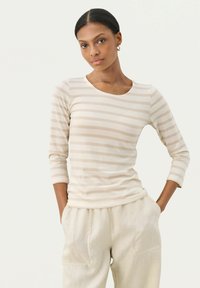 Beige og creme stribet langærmet bluse med rund hals og tætsiddende design. Kombineret med lyse, løst siddende bukser.
