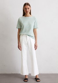 Gestreiftes Kurzarm-Oberteil in Hellblau und Weiß, kombiniert mit weißen Schlagjeans und schwarzen Flip-Flops. Einfaches, lässiges Design und Texturen.