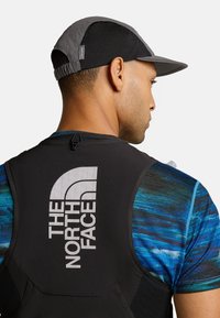 Gilet nero con logo "The North Face", tessuto texturizzato, camicia blu e nera a fantasia e un berretto grigio scuro. Dettaglio hardware notevole sul retro.