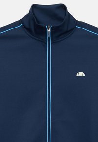 Marineblå zip-up jakke med lyseblå piping på skuldre og glidelås, høy krage og liten hvit halvmåne-logo på brystet.