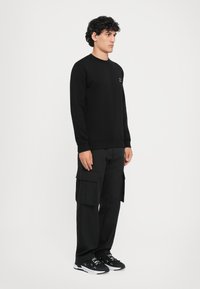 Sweatshirt preto com punhos canelados, combinado com calças cargo pretas de corte largo com bolsos laterais. Usado com sapatilhas pretas.