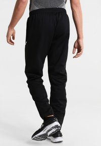 Pantalons de sport noirs avec une coupe ajustée, taille élastique et poches latérales. Fabriqués en tissu lisse et durable. Présente un accent logo.
