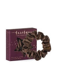 Brązowa jedwabna gumka do włosów prezentowana na wycięciu w kształcie gwiazdy na głębokim fioletowym pudełku z złotym napisem i wzorem gwiazd. Charakteryzuje się teksturowanym, luksusowym wykończeniem.