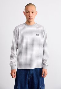 Langermet skjorte i grå og hvite striper, laget av myk bomull, med rund hals og en liten logo-lappe på brystet.