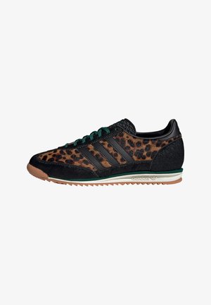 Zapatillas negras con acentos de estampado de leopardo, materiales texturizados, cordones verdes y una suela de goma marrón, que cuentan con tres franjas laterales negras.