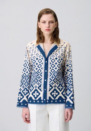 Chemise à manches longues crème et bleue avec des motifs géométriques, fermeture à boutons, col contrasté et ourlet à franges. Texture de tissu lisse.