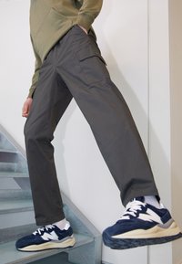 Grå cargo-byxor med sidofickor, kombinerat med marinblå och vita sneakers med texturerat ovandel och tjock sula, på en trappbakgrund.