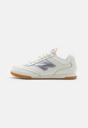 Biały niski sneaker z srebrnym logo po boku, białymi sznurowadłami i gumową podeszwą, pokazany z profilu zwrócony w lewo.