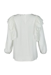 Valkoinen paita, jossa on tekstuuri kangas ja röyhelöhihat. Takana sijaitsee avaus, jossa on avainreiän muotoinen aukko kaulassa, yksinkertainen ja rento muoto.