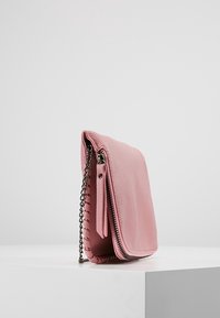 Borsa a tracolla rosa in pelle con superficie texturizzata, tracolla a catena, chiusura con cerniera e cuciture decorative lungo il bordo.