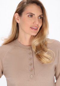 Top bej tricotat cu decolteu rotund, având o deschidere cu nasturi pe față și detalii subtile cu model în rib la guler și la mâneci.
