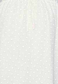 Tissu blanc avec un motif texturé de petits pois ronds blancs. Dispose d'un cordon de serrage au niveau du col pour un ajustement réglable.