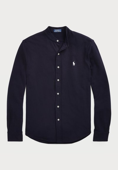Ναυτικό μπλε πουκάμισο μακρύ μανίκι με λουρί, κουμπιά μπροστά και ένα μικρό άσπρο έμβλημα αλόγου στο αριστερό στήθος. Φτιαγμένο από μαλακό ύφασμα.