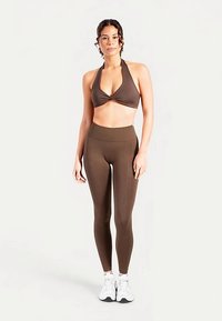 Reggiseno sportivo marrone e leggings a vita alta, realizzati in materiale elastico, con design a collo all'americana e texture liscia.