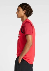 Camiseta deportiva roja de manga corta, con detalles negros en los costados. La tela parece texturizada, adecuada para ropa deportiva.