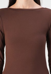 Brun ribbet langermet topp med bred båtformet hals. Glatt tekstur med vertikale linjer, tettsittende design og minimale sømdetaljer.