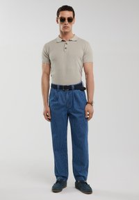 Šviesiai smėlinis trumpas rankovės polo marškinėliai, tamsiai mėlynų dryžuotų kelnių, mėlyni batai, akiniai nuo saulės ir rudas diržas. Dryžuotos kelnės yra laisvo kirpimo.