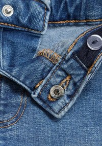 Modra denim tkanina s bližnjim posnetkom ovratnika, ki vključuje srebrne gumbne dele, oranžno šivano in teksturirano površino.