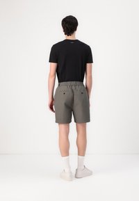 Maglietta nera, pantaloni corti grigi con vita elasticizzata, tasche frontali piatte e tasche posteriori con bottone. Calze bianche alla caviglia e scarpe.