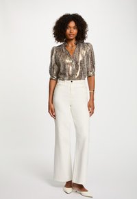Blouse à motif métallisé avec des manches bouffantes, associée à un pantalon large blanc à taille haute et des escarpins crème à bout pointu.
