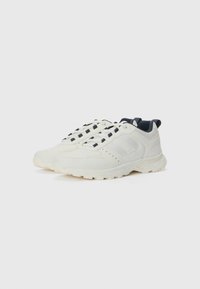 White athletic shoes with textured synthetic material, contrasting dark navy accents, lace-up design, and rugged sole for traction.