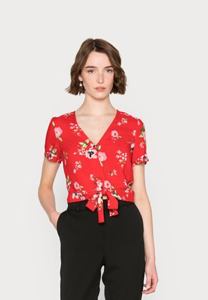 Blusa floral vermelha com mangas curtas, decote em V e detalhe de laço na frente. Apresenta pequenos padrões florais multicoloridos sobre um fundo sólido.