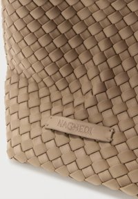 Μπεζ υφαντό υφασμάτινο τσάντα με υφή στην επιφάνεια, με ορθογώνιο σχήμα και εγχάρακτη ετικέτα της μάρκας, προσθέτοντας μια διακριτική σχεδιαστική λεπτομέρεια.