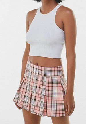 Kvinde iført en hvid ribbet ærmeløs crop top og en lyserød ternet plisseret mini nederdel, stående mod en ensfarvet baggrund.