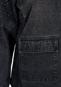 Černá denimu látka s texturovaným povrchem, s malými stříbrnými a modrými cvočky uspořádanými v rozptýleném vzoru. Obsahuje zadní kapsu.