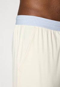 Pantaloni sportivi beige chiaro con una cintura elastica a motivo blu chiaro e tasche laterali, realizzati in tessuto morbido e leggero.
