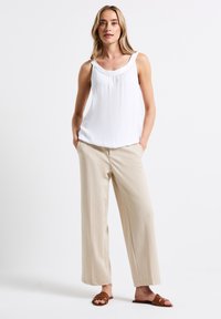 Top blanco sin mangas con escote fruncido, combinado con pantalones de pierna ancha beige y sandalias marrones. Presenta una tela suave y un ajuste relajado.