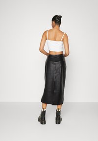 Kvinna som står med ryggen mot kameran, iförd en vit crop top, svart läder midi kjol och svarta snörkängor med vita strumpor.