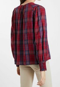 Chemise à carreaux rouge et bleu avec de longues manches bouffantes, dotée de poignets élastiques et d'une petite ouverture à l'arrière. Matière en coton avec une finition texturée.