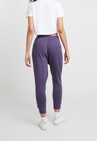 Lila joggers med elastisk midjeband och fållade benslut. Har en enda bakficka och slät bomullsmateriel. Minimalistisk design.