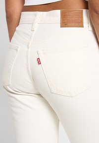 Vaqueros de mezclilla blanca con un acabado texturizado, que cuentan con bolsillos traseros y una etiqueta marrón de Levi's en la cintura.