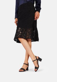 Gonna in pizzo nero con orlo a campana e un paio di sandali con tacco in pelle nera con cinturini alla caviglia e design open toe.