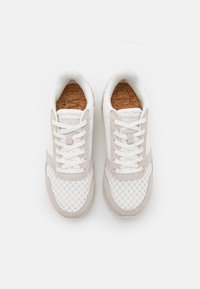 Lehká sportovní obuv se bílou síťovinou a béžovými semišovými akcenty, texturovanými korkovými stélkami a bílými tkaničkami. Zaoblený tvar špičky.