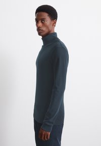 Donkerblauwe coltrui in een slim fit. Heeft lange mouwen, een gladde textuur en minimale stikseldetails. Gepaard met marineblauwe corduroy-broeken.