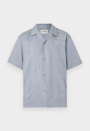 Chemise bleu clair à manches courtes avec deux rangées verticales de volutes abstraites brodées en blanc sur les côtés avant.