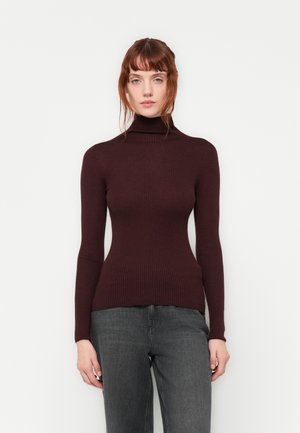 Ribbet, tettsittende høyhalset genser i mørk burgunder. Myk tekstur med lange ermer, kombinert med grå jeans. Enkelt, strømlinjeformet design.
