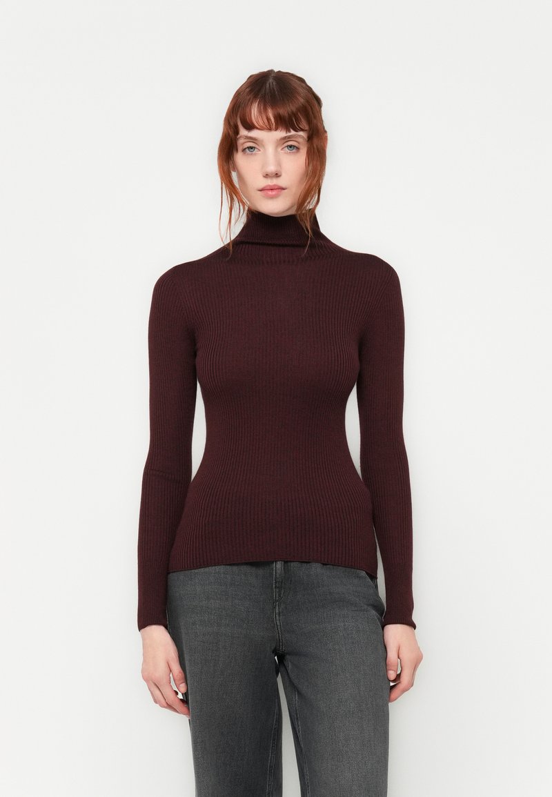 Rippent, taillierter Rollkragenpullover in dunklem Burgunderrot. Weicher Stoff mit langen Ärmel, kombiniert mit grauen Jeans. Schlichtes, geradliniges Design.