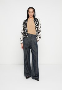 Cardigan à motif zèbre noir et beige porté sur un haut beige, associé à un pantalon en denim foncé à taille haute et jambes larges, et des chaussures noires.