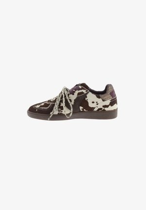 Zapatilla baja con patrón de estampado de vaca en marrón y blanco, cordones blancos y negros salpicados, y suela y detalles en el talón de color marrón oscuro.