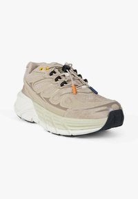 Scarpa da ginnastica beige con tomaia in mesh e camoscio, lacci neri e arancioni, suola bianca ammortizzata con suola esterna nera texturizzata.